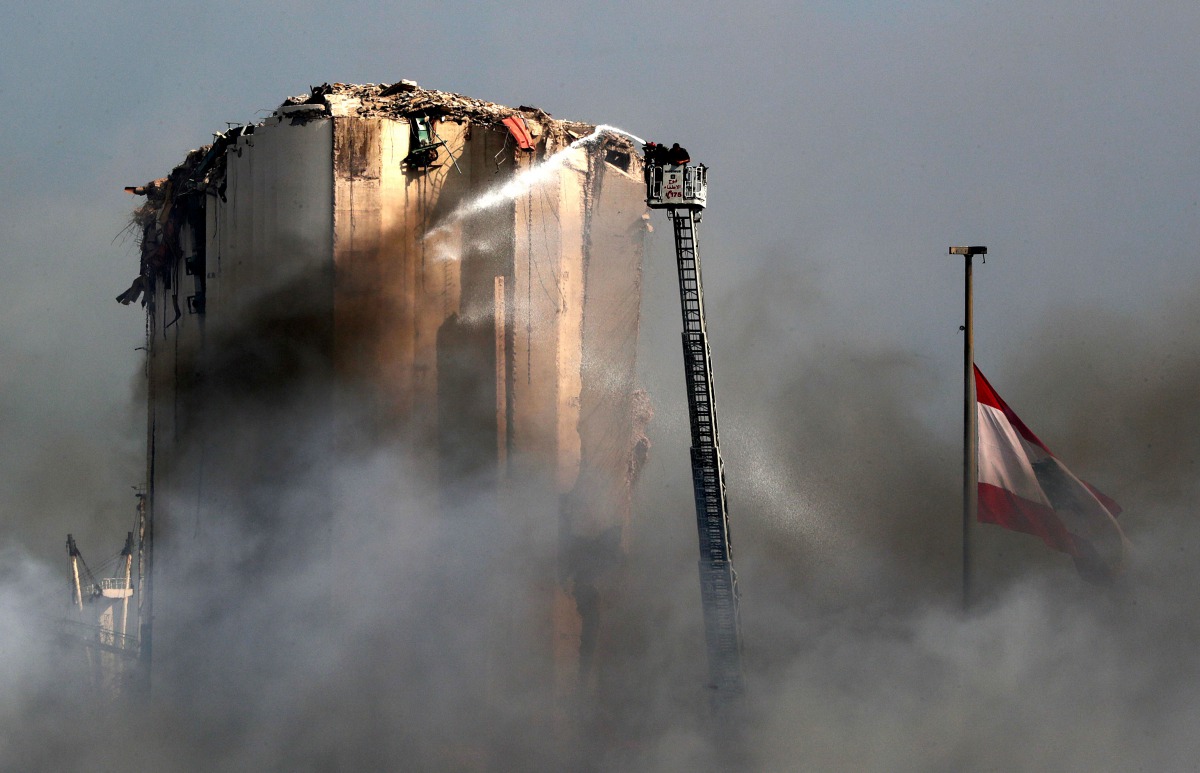 Lebanese firefighters stand on a ladder amid billowing smoke as they extinguish the remaining flames at the seaport of Beirut, on September 11, 2020, a day after a huge fire erupted in harbour warehouses. / AFP / ANWAR AMRO
