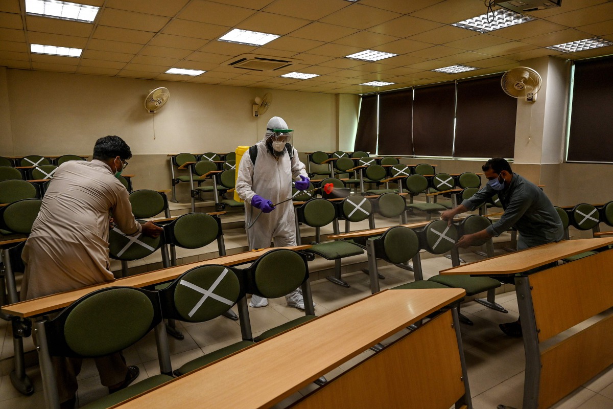 A worker wearing a Personal Protective Equipment (PPE) suit (C) sprays disinfectant while other workers tag cross signs on chairs for social distancing at the Capital University of Science and Technology in Islamabad on September 10, 2020, following the g