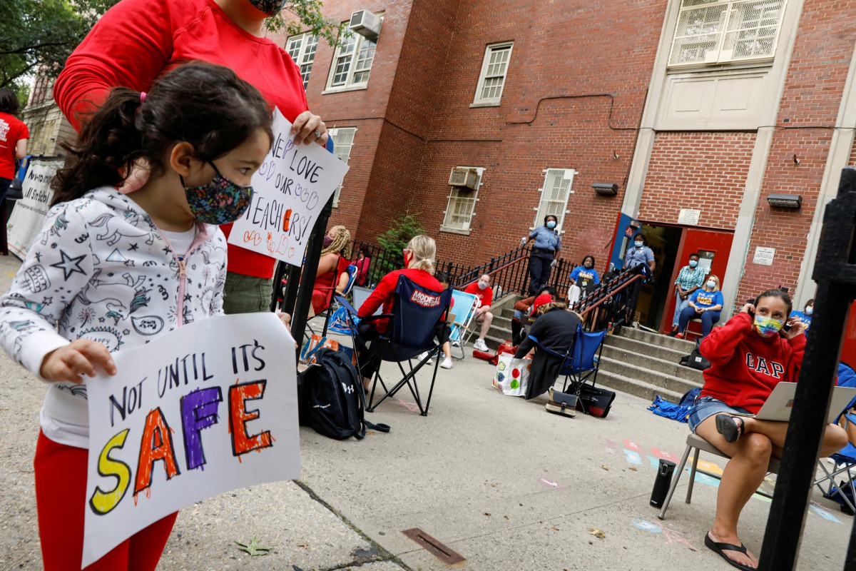 A parent and a child carry signs to protest the opening of schools, as teachers work outside their school building for safety reasons, following the outbreak of the coronavirus disease (COVID-19) in the Brooklyn borough of New York City, U.S., September 1