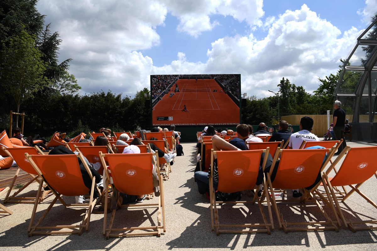 (FILES) In this file photo taken on May 29, 2019 people sit in sun loungers outside of the courts and watch on a giant screen the men's singles second-round match between Greece's Stefanos Tsitsipas and Bolivia's Hugo Dellien on day four of The Roland Gar
