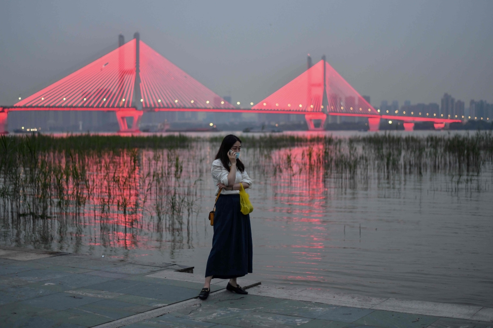 A woman wearing a face mask as a preventive measure against the Covid-19 coronavirus talks on her phone next to the Yangtze River in Wuhan, in China’s central Hubei province on September 25, 2020. / AFP / Hector RETAMAL