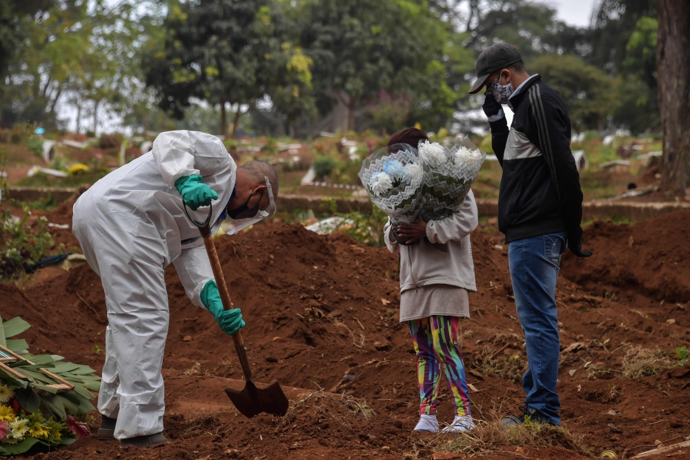 An employee digs next to relatives of a person who died from COVID-19 at the Vila Formosa cemetery, in the outskirts of Sao Paulo, Brazil.  AFP / NELSON ALMEIDA
