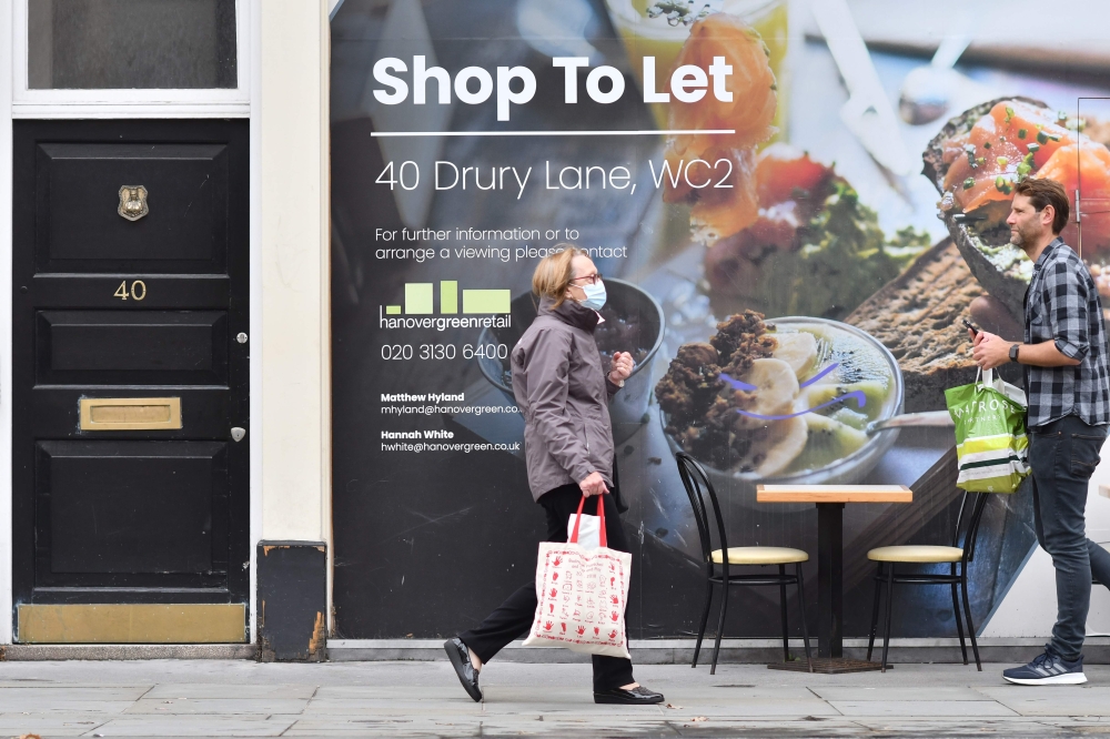 A pedestrian wearing a face mask as a precaution against the transmission of the novel coronavirus walks past a boarded up shop front which is to let in central London on October 13, 2020.  AFP / JUSTIN TALLIS