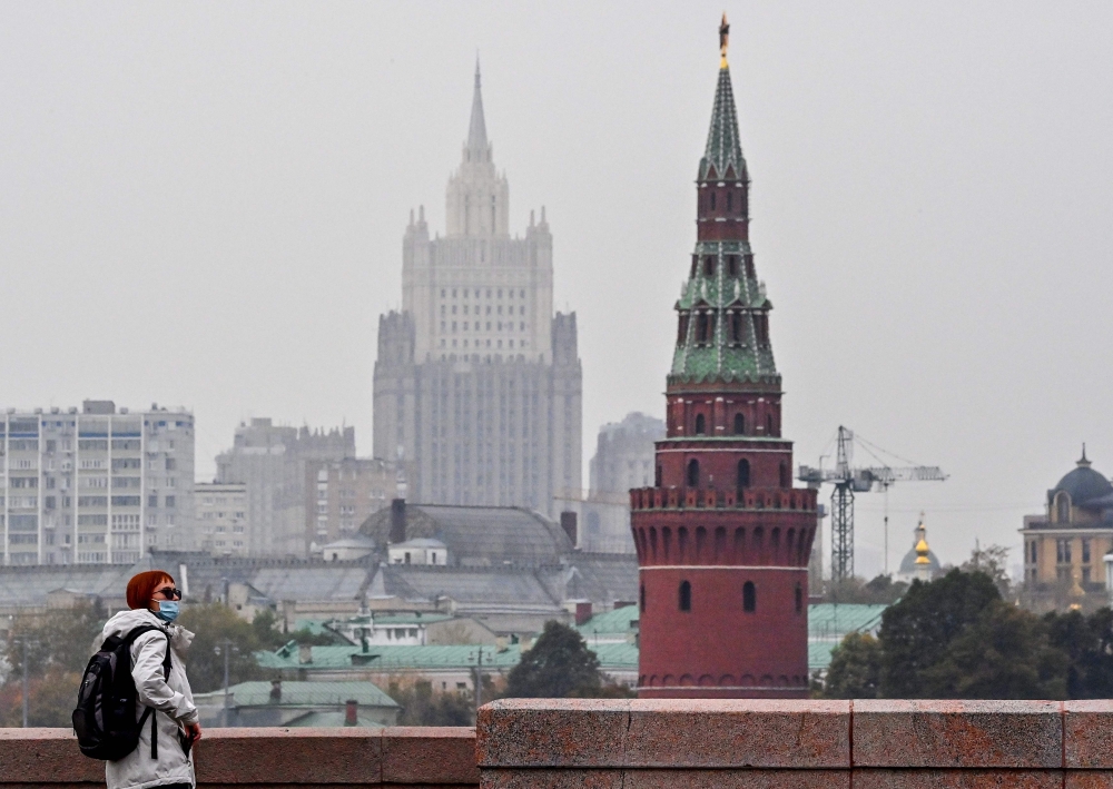 A woman wearing a face mask to protect against the coronavirus disease walks along a bridge in front of a tower of the Kremlin and the Russian Foreign Ministry building on the background in central Moscow on October 13, 2020. / AFP / Yuri KADOBNOV