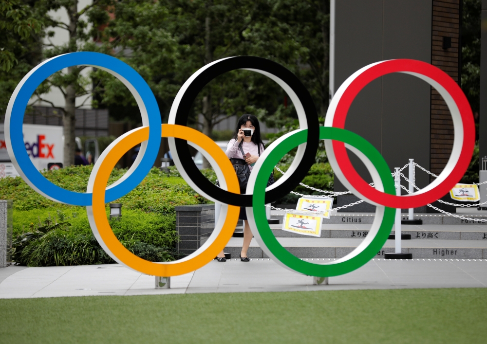 A woman wearing a protective mask amid the coronavirus disease (COVID-19) outbreak, takes a picture of the Olympic rings in front of the National Stadium in Tokyo, Japan October 14, 2020. REUTERS/Kim Kyung-Hoon