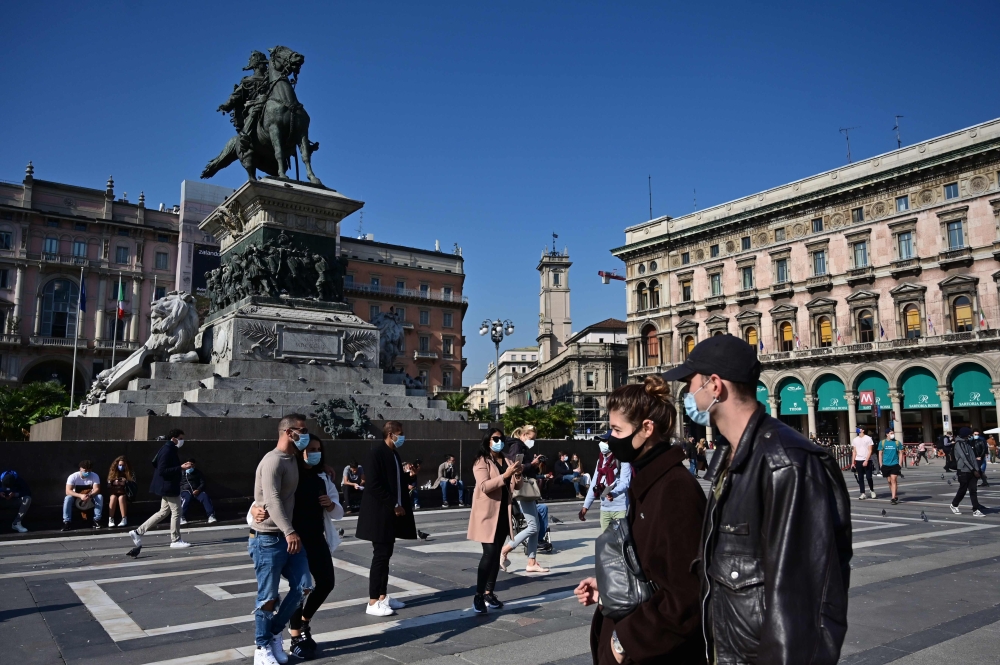 People wearing protective masks walk across the Piazza del Duomo in Milan on October 17, 2020, amid the Covid-19 pandemic. AFP / MIGUEL MEDINA