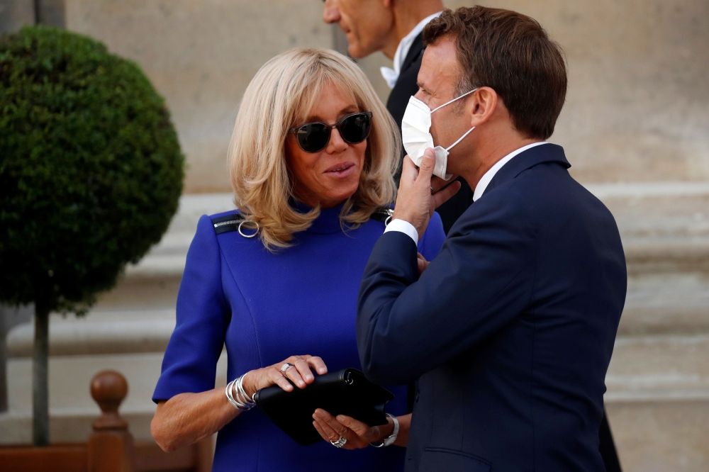In this file photo taken on July 13, 2020, French President Emmanuel Macron wearing a face mask speaks with his wife Brigitte Macron after giving a speech to France's armed forces at the Hotel de Brienne, the French Ministry of Armed Forces, in Paris. Bri