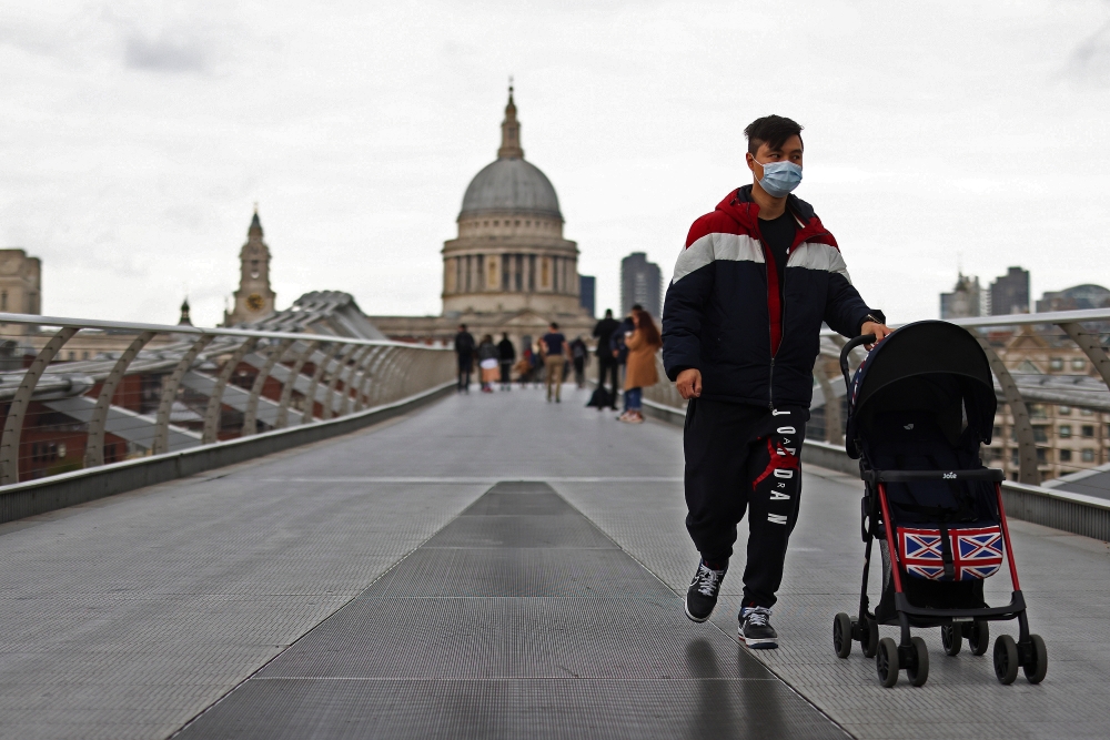 A man pushing a pram crosses Millennium Bridge in view of St Paul's Cathedral as the coronavirus disease (COVID-19) outbreak continues in London, Britain October 18, 2020. Reuters/Simon Dawson
 