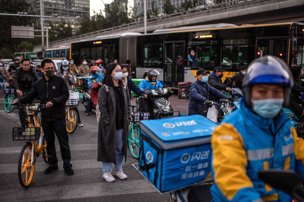 A woman (C) wearing a face mask as a preventive measure against the Covid-19 coronavirus waits to cross a street during rush hour in Beijing on October 21, 2020. AFP / Nicolas Asfouri 