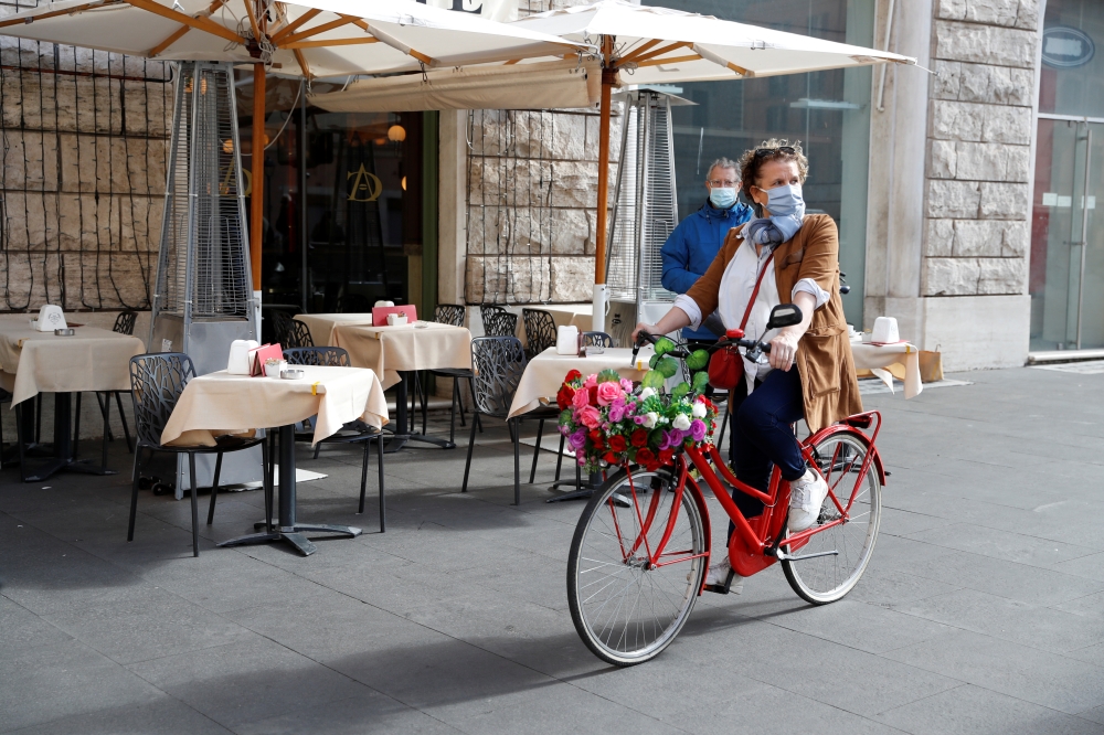 A woman wearing a protective face mask rides a bicycle past a restaurant as the outbreak of the coronavirus disease (COVID-19) continues, in Rome, Italy, October 25, 2020. REUTERS/Yara Nardi