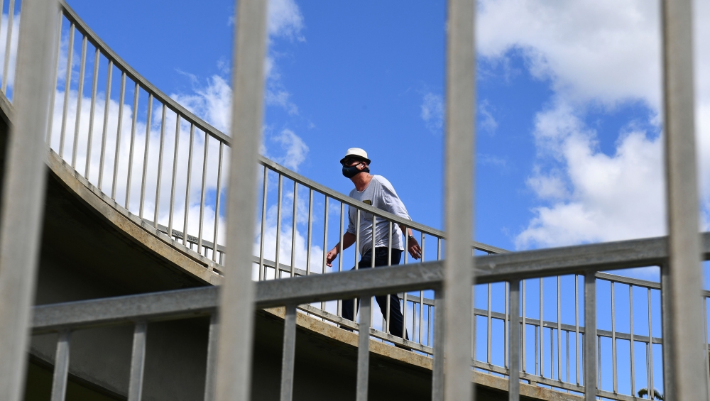 A man wearing a face mask crosses a pedestrian bridge in the Melbourne suburb of St Kilda on October 26, 2020 as Australian health officials reported no new coronavirus cases or deaths in Victoria state, which has spent months under onerous restrictions a