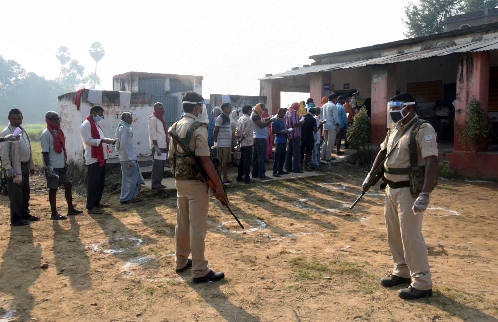 Policemen wearing protective face shields stand guard as voters stand in a queue to cast their vote outside a polling booth during the state assembly election, amidst the spread of the coronavirus disease (COVID-19), at a village on the outskirts of Patna