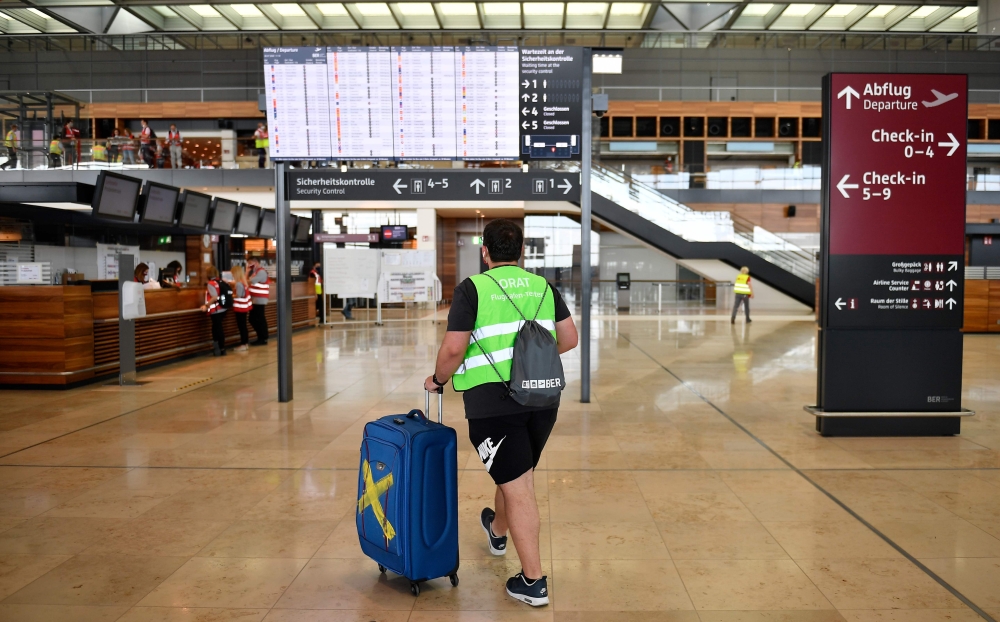 (FILES) This file photo taken on July 30, 2020, shows a volunteer walking in front of the departure information board during a test run at the Berlin-Brandenburg Willy-Brandt international Airport (BER) in Schoenefeld near Berlin.  AFP / Tobias Schwarz 
