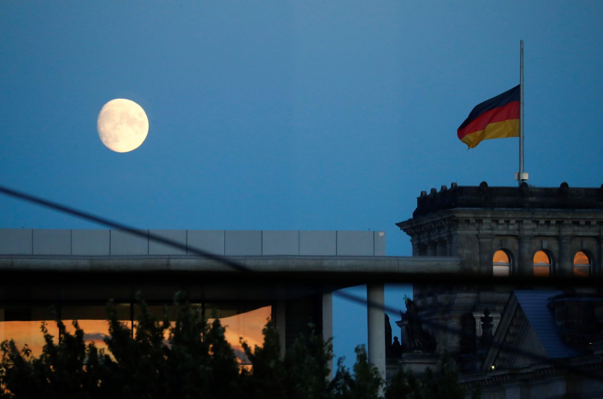The moon is seen beside the Reichstag, the building which houses the Bundestag (lower house of parliament), from the Chancellery in Berlin before a news conference on new coronavirus restrictions following consultations with the premiers of Germany's 16 f