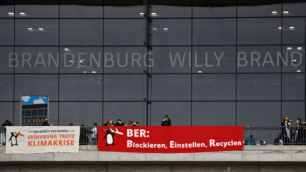 Climate activists hang banners reading 'opening despite climate crisis' (L) and 'BER : Block, Erase, Recycle' in front of the main Terminal of Berlin's airport 