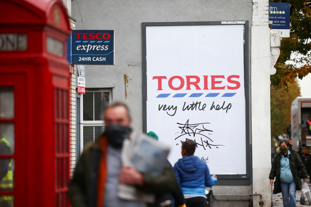 People walk past a poster by artist Hayden Kay, amid the coronavirus (COVID-19) outbreak, in London, Britain, October 30, 2020. REUTERS/Henry Nicholls