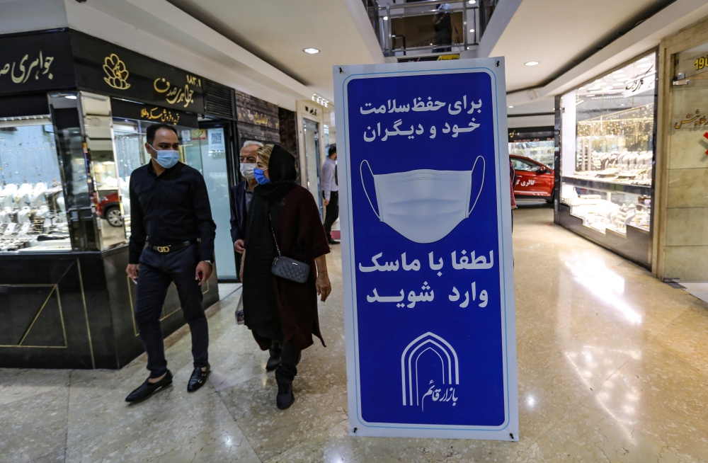 Iranians walk next to a sign advising people to wear masks on their way to shop in Tajrish square in the capital Tehran on November 1, 2020, amid the novel coronavirus pandemic crisis. / AFP / ATTA KENARE
