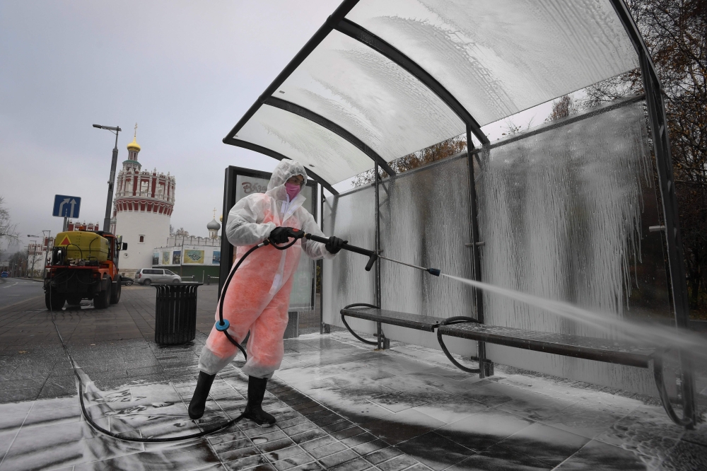 A municipal worker wearing protective equipment sprays disinfectant on a bus stop near the Novodevichy convent in Moscow on November 3, 2020, amid the ongoing coronavirus disease pandemic. / AFP / Natalia KOLESNIKOVA