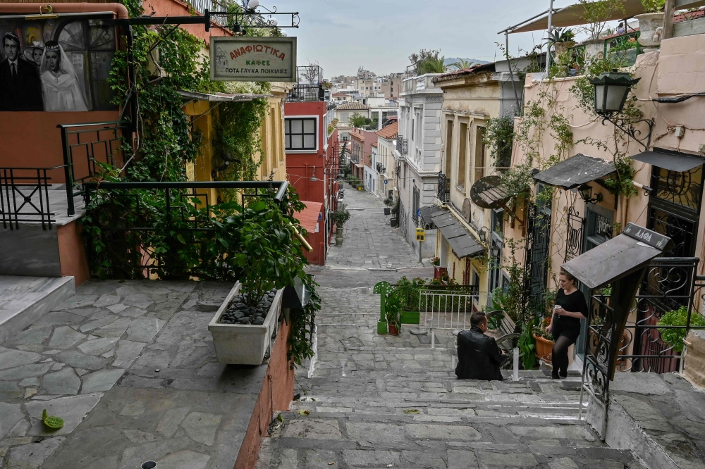 People talk while standing by empty terraces in Plaka district of central Athens as cafes bars and restaurants close due to a partial lockdown to stem the spread of the novel coronavirus, Covid-19, on November 3, 2020. / AFP / LOUISA GOULIAMAKI