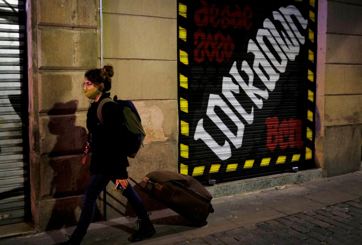 A woman wearing a face mask pushes her suitcase on a street, after Catalonia's government imposed new restrictions in an effort to control the spread of the coronavirus disease (COVID-19), in Barcelona, Spain October 29, 2020. REUTERS/Nacho Doce

