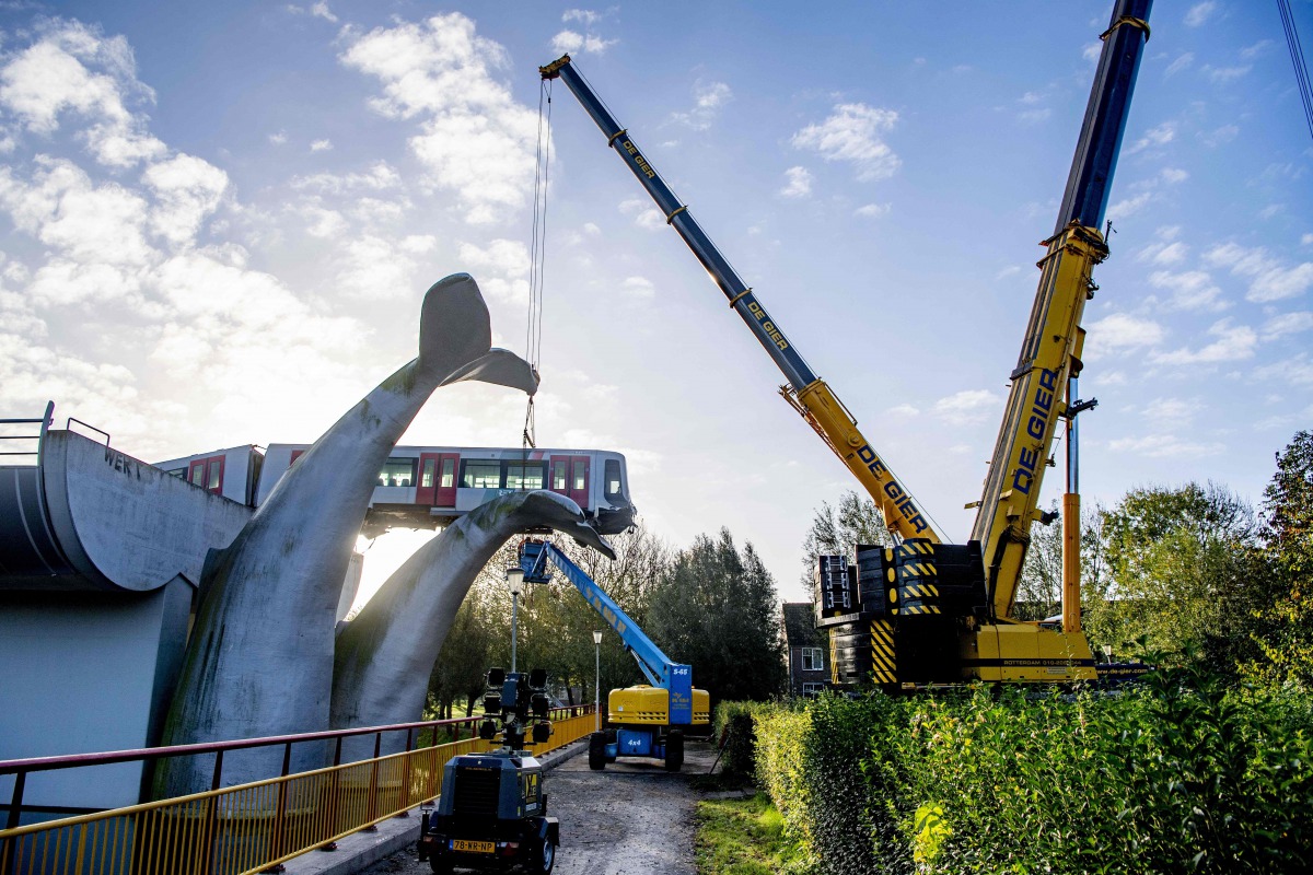 TOPSHOT - Workers use a crane to the salvage a metro train after it overran a barrier at De Akkers station in Spijkenisse on November 3, 2020. and ended up suspended on a work of art in the shape of a large whale's tail. / AFP / ROBINUTRECHT / ANP / Robin