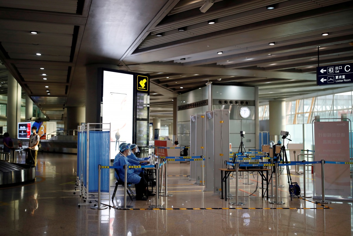 FILE PHOTO: Staff members in protective suits sit at a checkpoint at Beijing Capital International Airport, following new cases of the coronavirus disease (COVID-19) infections, in Beijing, China June 16, 2020. REUTERS/Carlos Garcia Rawlins/File Photo
