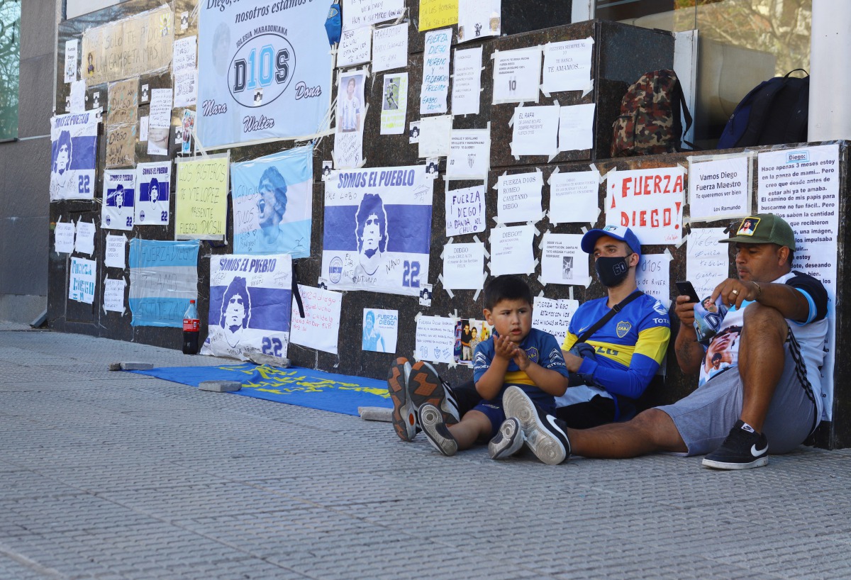 Fans of Argentine soccer great Diego Maradona sit next to a wall filled with encouraging messages outside the clinic where Maradona underwent brain surgery, in Olivos, on the outskirts of Buenos Aires, Argentina November 5, 2020. REUTERS/Matias Baglietto