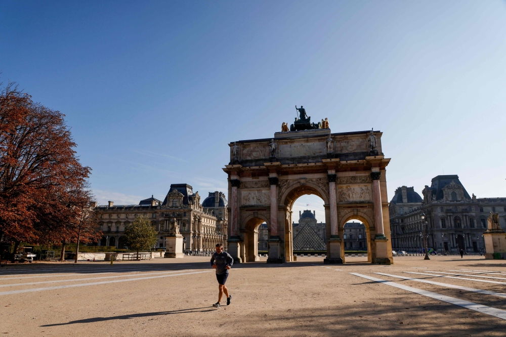 A jogger runs in front of Arc de Triomphe du Carrousel in Paris on November 6, 2020, during a lockdown imposed by authorities in an attempt to halt the spread of the new coronavirus (Covid-19). AFP / Ludovic Marin 