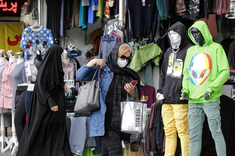 A woman, mask-clad due to the COVID-19 coronavirus pandemic, browses a phone as she walks past a shop along a street in Iran's capital Tehran on November 8, 2020. / AFP / ATTA KENARE