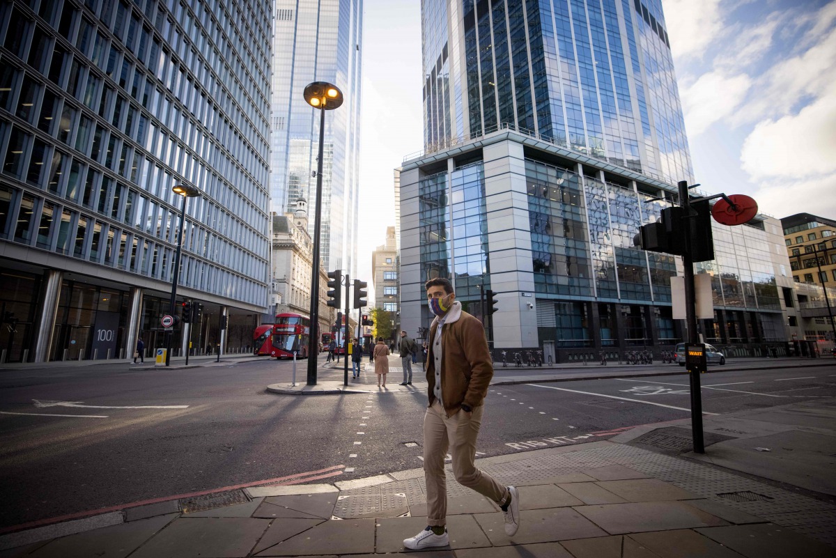 A man wearing a protective face covering to combat the coronavirus walks along a quiet street in the City of London on November 10, 2020.  / AFP / Tolga Akmen
