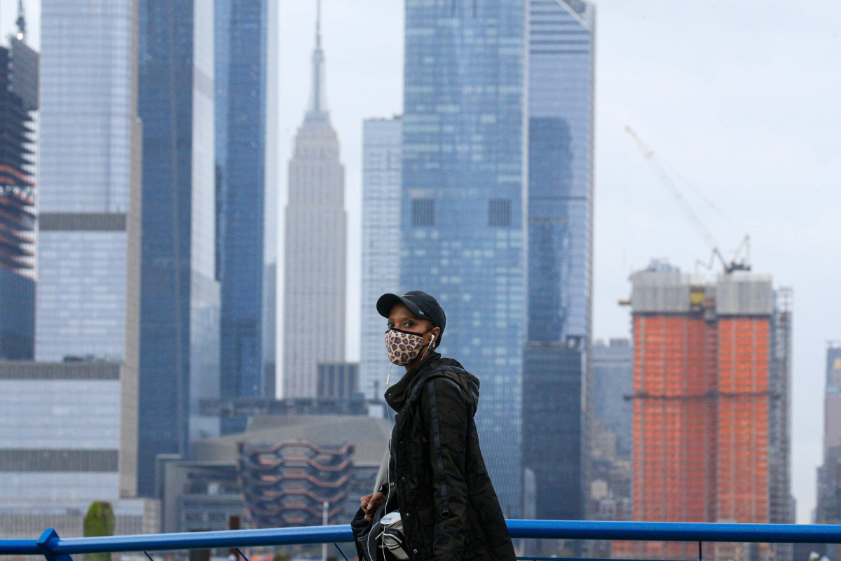 A person wearing a face mask walks in Weehawken, New Jersey, on November 11, 2020, with the New York skyline in the background. Mayor Bill de Blasio said November 9 that New York City is getting “dangerously close” to a second coronavirus wave as the infe