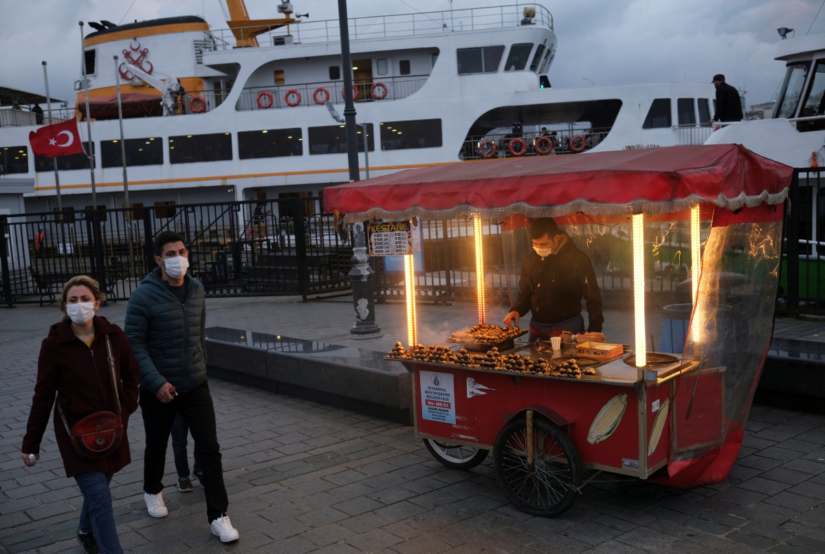 People wearing protective masks walk past by a street vendor selling roasted chestnuts, amid the spread of coronavirus disease (COVID-19), in Istanbul, Turkey November 10, 2020. REUTERS/Murad Sezer
