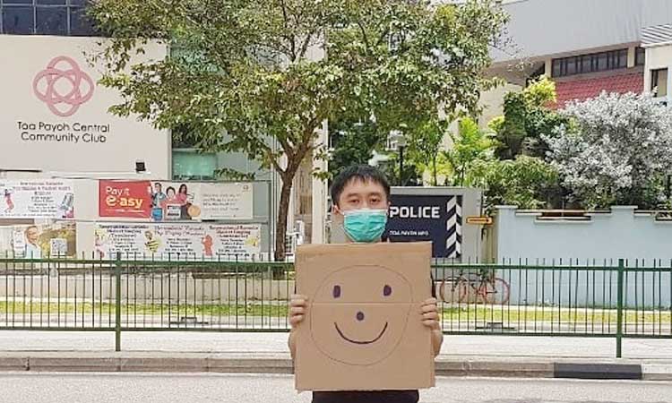 Jolovan Wham wears a mask and holds a cardboard with a drawing of a smiley face in Singapore, March 28, 2020. Picture taken March 28, 2020. Jolovan Wham/Handout via REUTERS 