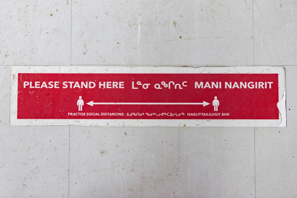 A sign written in English and Inuktitut requesting social distancing to help slow the spread of coronavirus disease (COVID-19) is seen on the floor of a grocery store as the territory of Nunavut enters a two week mandatory restriction period in Iqaluit, N