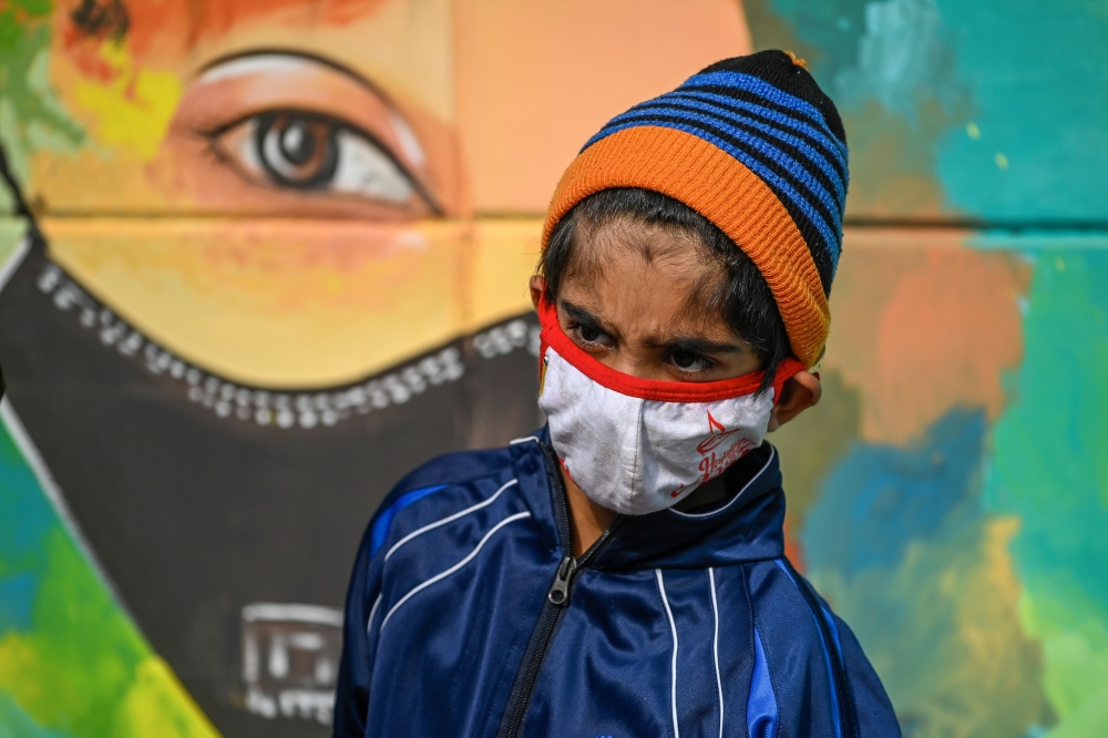A boy wearing a facemask as a preventive measure against the Covid-19 coronavirus walks past a mural in New Delhi on November 23, 2020. / AFP / Sajjad HUSSAIN
