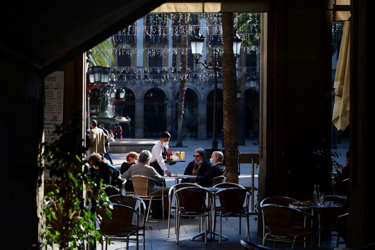 A waiter serves customers at a restaurant in Barcelona on November 23, 2020 as bars, restaurants and movie theatres were allowed to reopen in Spain's northeastern region of Catalonia after being closed for over a month as part of measures to slow coronavi