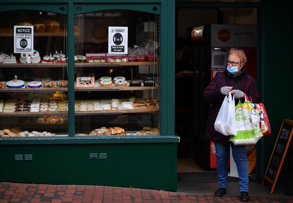 A customer wearing a face mask or covering due to the COVID-19 pandemic, carries her shoppingas she leaves a patisserie in Sittingbourne in the Swale district of Kent, south east England on November 24, 2020, which has become England's worst hit coronavir