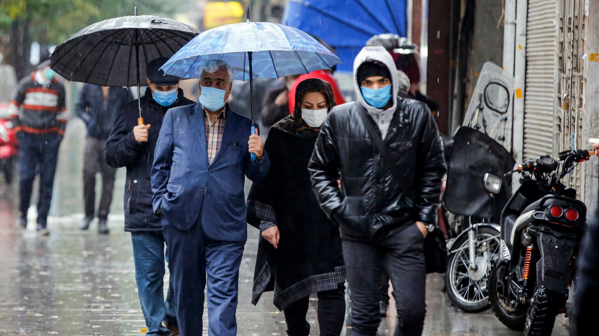 Pedestrians, clad in mask due to the COVID-19 coronavirus pandemic, walk in the rain past closed shops along a street in Iran's capital Tehran on November 21, 2020, as the Iranian government announced new pandemic-countering measures. / AFP / -
