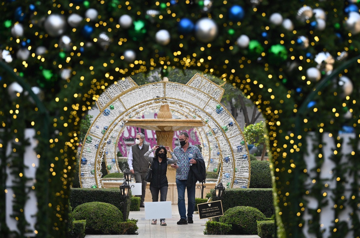 People wearing masks to prevent the spread of COVID-19 walk through a holiday season and Christmas outdoor display in Beverly Hills, California, November 23, 2020. / AFP / Robyn Beck
