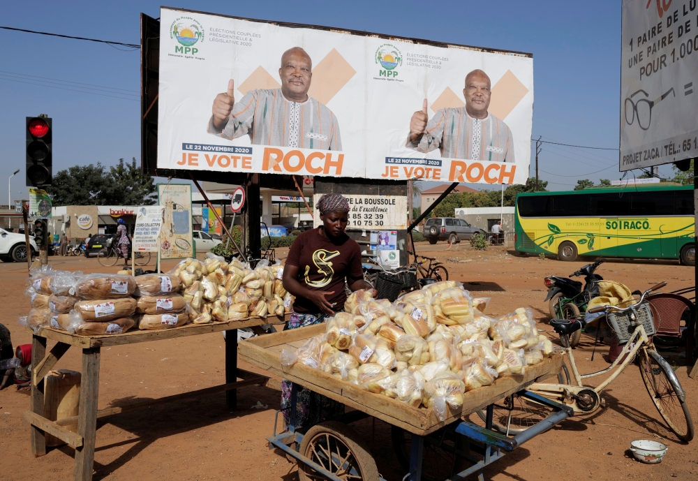 A woman displays bread for sale near a campaign banner of presidential candidate Roch Kabore in Ouagadougou, Burkina Faso November 20, 2020. REUTERS/Zohra Bensemra
