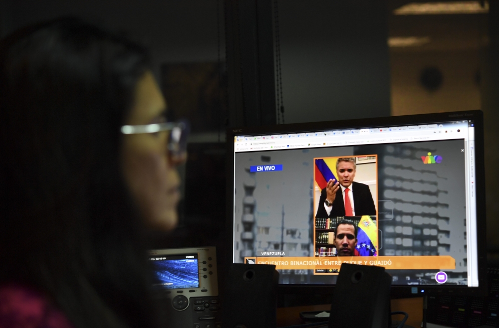 (FILES) In this file photo, a journalist follows the live online encounter between Colombian President Ivan Duque (top) and Venezuelan opposition leader and self-declared acting president Juan Guaido, on a computer in Caracas, on February 15, 2019. AFP / 