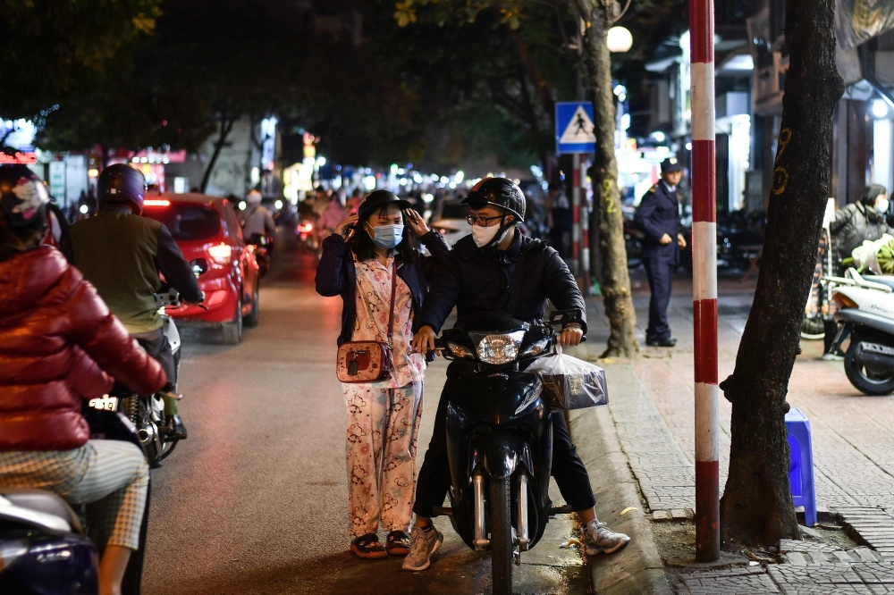 A woman (L) wearing a facemask adjusts her helmet along a street in Hanoi on December 1, 2020, a day after Vietnam reported its first local transmission case of Covid-19 in nearly three months. AFP / Manan Vatsyayan 