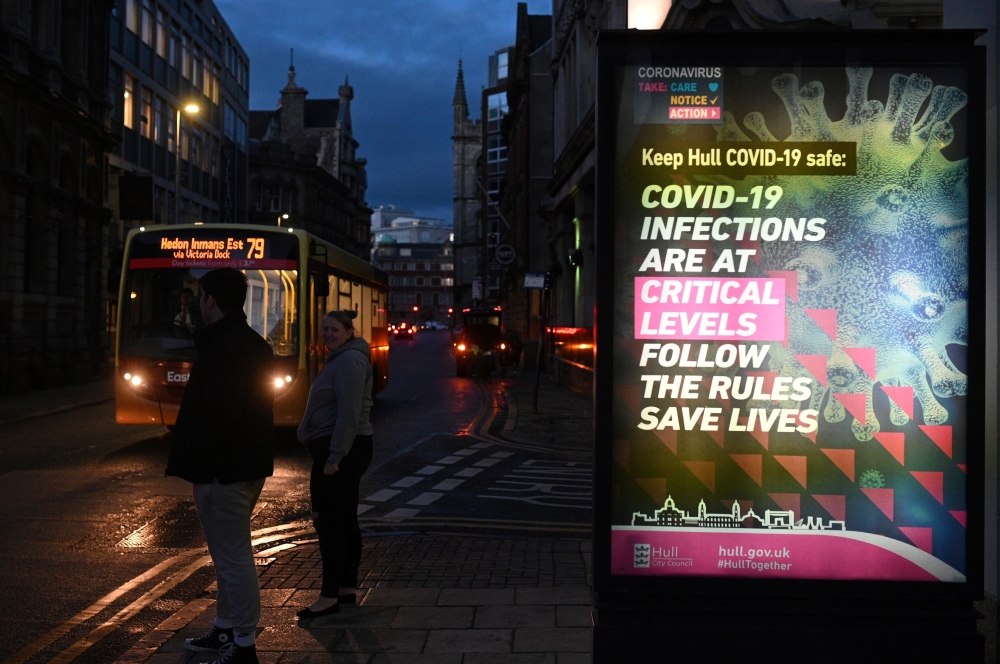 Pedestrians stand near a COVID-19 information board in Hull, in north-east England on November 30, 2020. Hull will return to the England's highest coronavirus category, Tier 3, when England exits its second lockdown an re-enters a tiered system of toughen