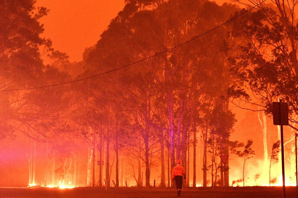 FILE PHOTO: A firefighter walks past burning trees during a battle against bushfires around the town of Nowra in the Australian state of New South Wales on December 31, 2019.  AFP / SAEED KHAN