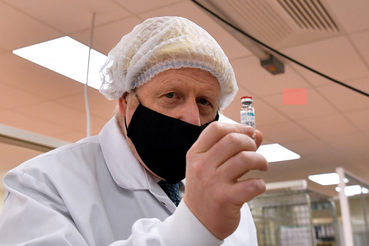Britain's Prime Minister Boris Johnson, wearing a hair net and face covering, poses for a photograph with a vial as he views the last minute quality testing of the 'fill and finish' stage of the manufacturing process of COVID-19 vaccines, Wales, Britain N