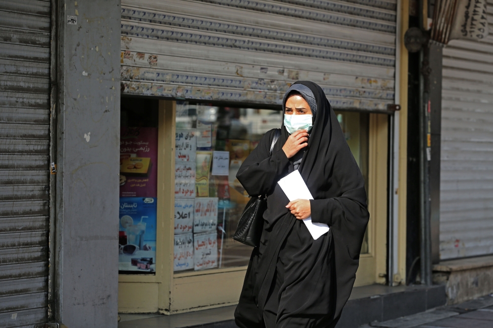 A woman wearing a face mask amid the COVID-19 pandemic walks by closed shops in the Iranian capital Tehran, on November 30, 2020. / AFP / ATTA KENARE