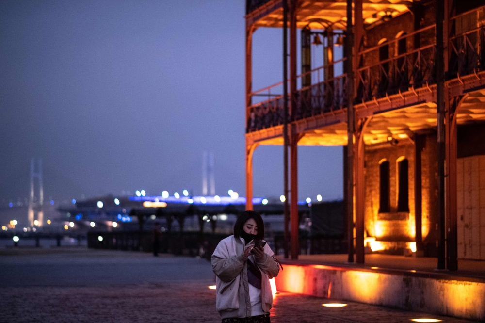 A woman looks at her mobile phone as she walks in Yokohama on December 3, 2020. / AFP / Philip FONG