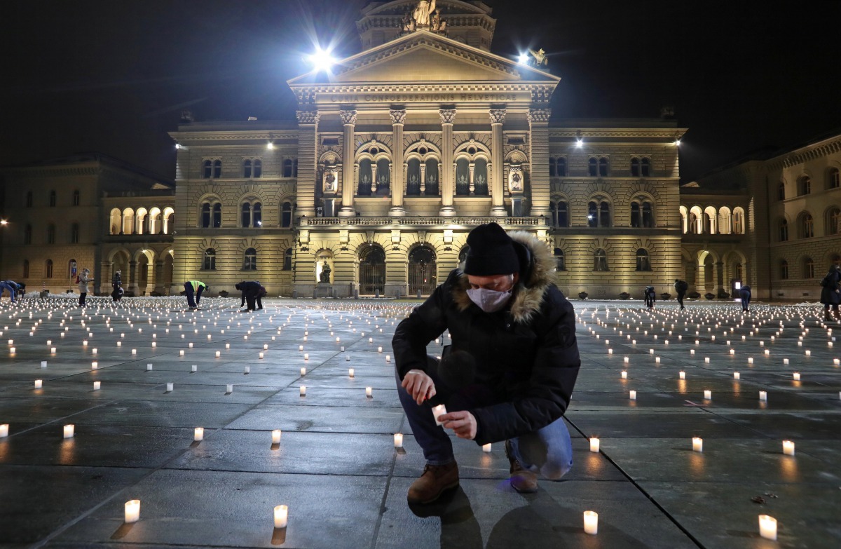 A man lights candles symbolizing the coronavirus disease (COVID-19) victims during a candlelight vigil on the Bundesplatz, in front of the seat of the Swiss federal parliament, Bundeshaus, in Bern, Switzerland December 6, 2020. Picture taken December 6, 2
