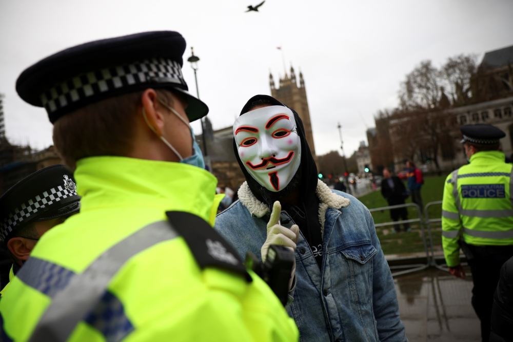 A person wearing mask talks with a police officer during an anti-vaccination demonstration at Parliament Square in London, Britain, December 14, 2020. REUTERS/Henry Nicholls