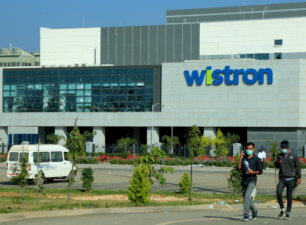 File photo: Men wearing protective face masks walk past broken windows of a facility run by Wistron Corp, a Taiwanese contract manufacturer for Apple, in Narsapura near the southern city of Bengaluru, India, December 14, 2020. Reuters/Stringer/File Photo